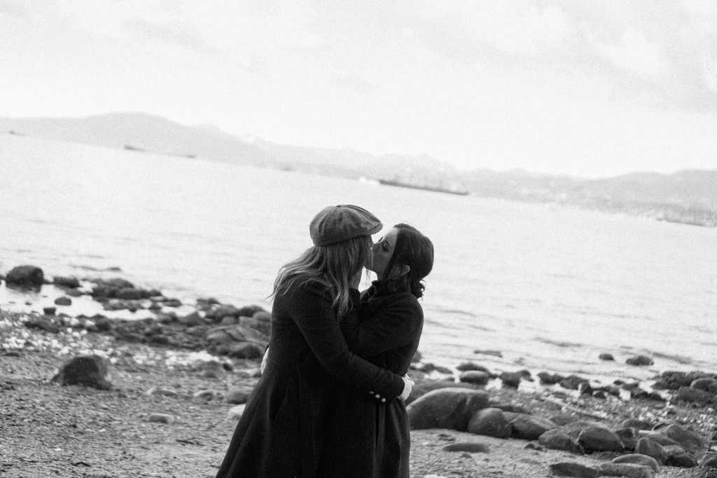 Joyful lesbian couple kissing on a Vancouver beach after a marriage proposal — intimate engagement photo capturing love and celebration by the ocean