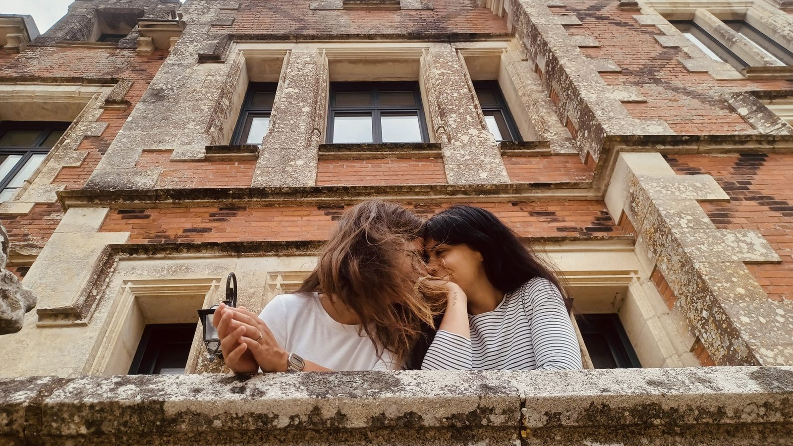 Lesbian couple sharing a quiet moment on the balcony of a French château – romantic LGBTQ+ wedding photography in the French countryside