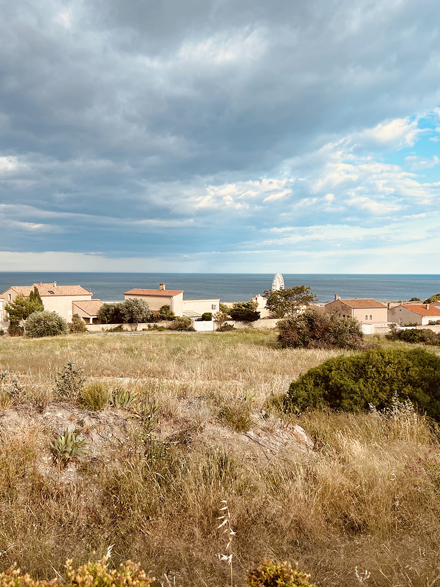 Warm and windy scenery of the South of France with dry fields and a quaint village in the distance — capturing the peaceful charm of rural French life