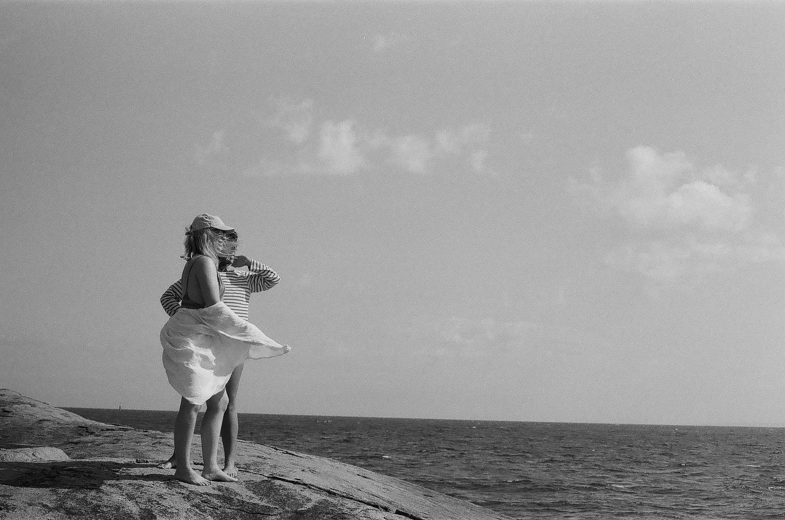 black and white film shot of 2 friends standing on a big rock, looking at the ocean